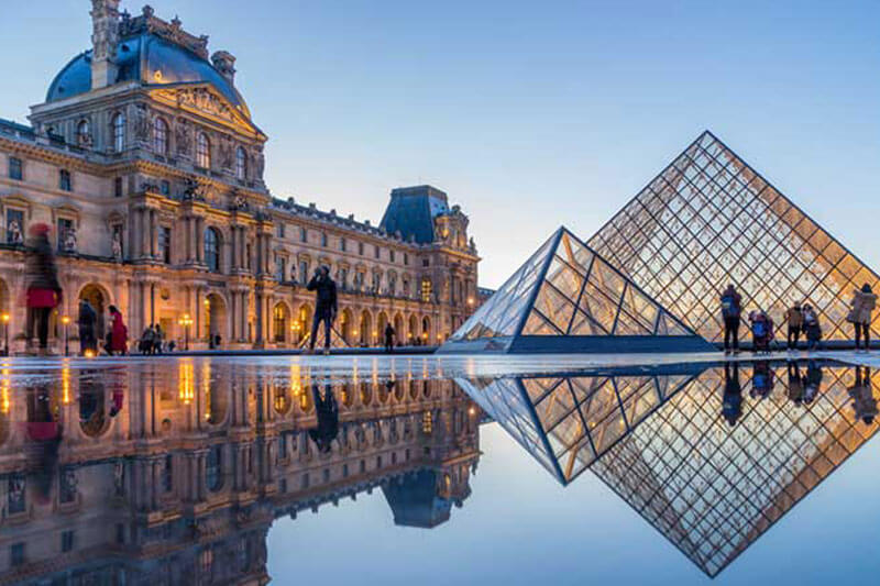 Tampak luar The Louvre di Paris saat sore hari dan dipenuhi turis.